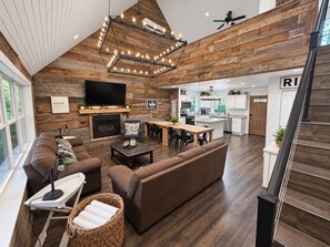 A spacious living area with a fireplace, a television, and a dining area with a kitchen in the background.