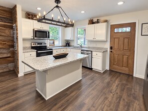 A modern kitchen with white cabinetry, a granite countertop, and a wooden floor.