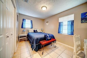 A bedroom with a bed, bench, bedside tables, and a chair. - Joys Beach House (Panama City Beach)