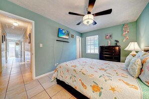 A bedroom with a bed, a ceiling fan, a TV, a dresser, and a window. - Joys Beach House (Panama City Beach)