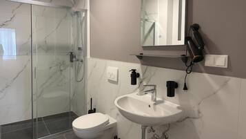 Ein modernes Badezimmer mit einer gläsernen Duschkabine, einem weißen Waschbecken und einer Toilette.