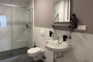 A modern bathroom with a glass-enclosed shower, a white sink, and a toilet. - HI Skyline Hotel (Hannover)