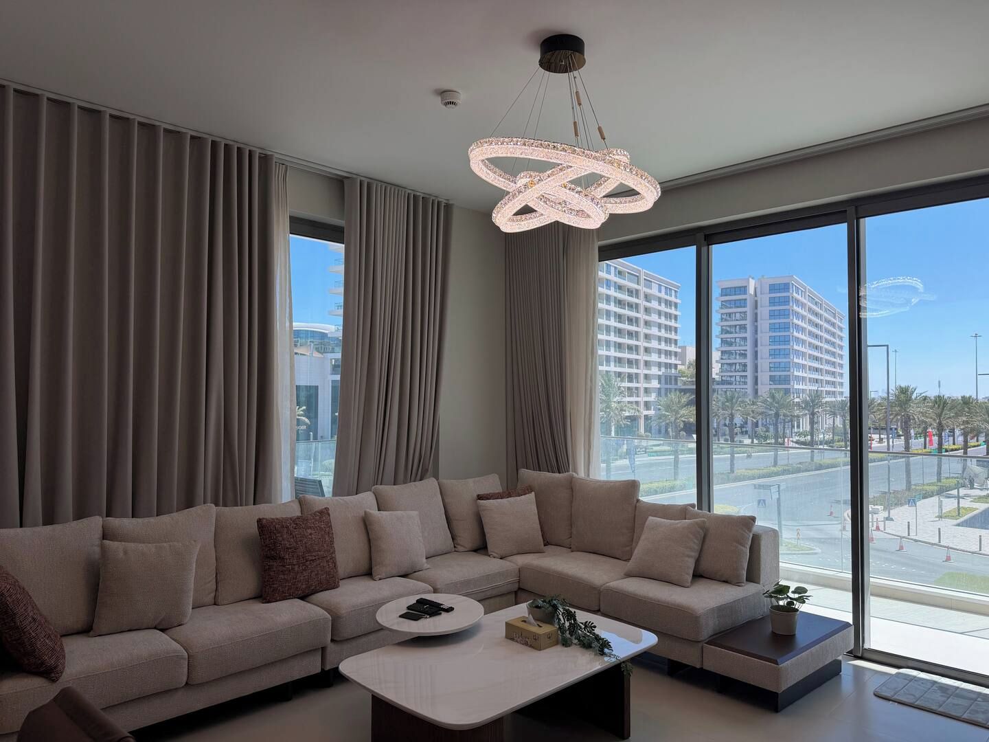 Ein modernes Wohnzimmer mit einer Eckcouch, einem runden Couchtisch und einem großen Fenster mit Blick auf eine Stadtlandschaft.