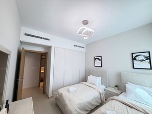 Habitación de hotel con dos camas, un armario, una mesita de noche con lámpara e iluminación en el techo.