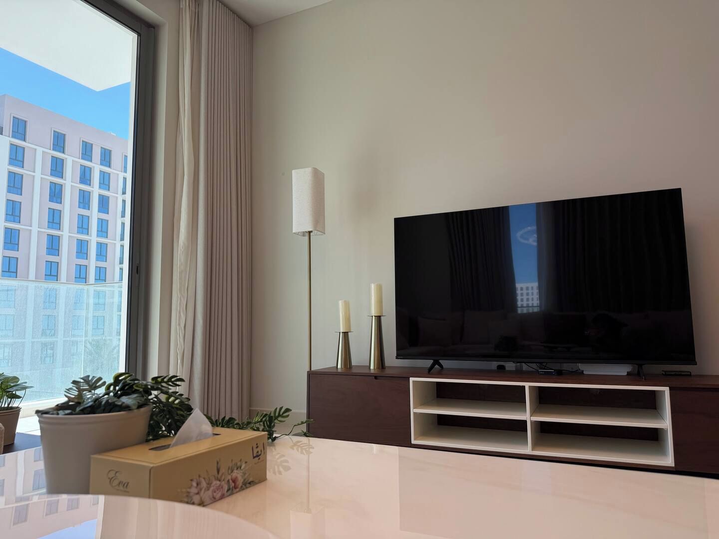 Ein modernes Wohnzimmer mit großem Flachbildfernseher, einer Stehlampe und einem Blumentopf.
