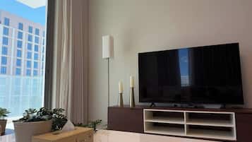 Ein modernes Wohnzimmer mit großem Flachbildfernseher, einer Stehlampe und einem Blumentopf.