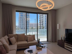 Una sala de estar moderna con un sofá, una mesa de centro, un televisor y un ventanal con vistas a rascacielos.
