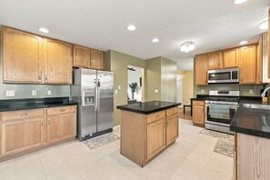 A modern kitchen with wooden cabinets, stainless steel appliances, and a black countertop. - 4 King Beds Premium Home in Mason (Mason)
