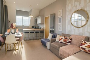 A modern living room with a sofa, a dining table with chairs, a kitchen area, and a large window. - The Stylish Artist Penthouse | Central Harrogate (Harrogate)