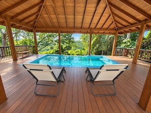 Eine Holzterrasse mit Pool, zwei Liegestühlen und einer Holzpergola.