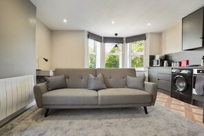 A modern living room with a sofa, a washing machine, and a kitchen area.