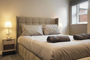 A bedroom with a bed, two bedside lamps, a window, and a nightstand.