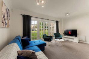 A living room with a blue sofa, two green armchairs, a coffee table, and a TV with the Netflix logo. - The York Haven | Stylish 4-Bed Sleeps 10 (York)