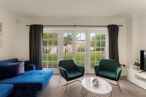 A room with a blue sofa, two green armchairs, a white coffee table, and a television on a white cabinet. - The York Haven | Stylish 4-Bed Sleeps 10 (York)