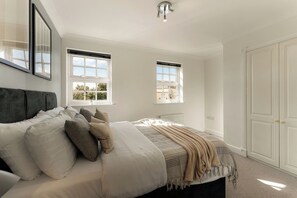 Een slaapkamer met een bed, twee ramen, een radiator en een kledingkast.