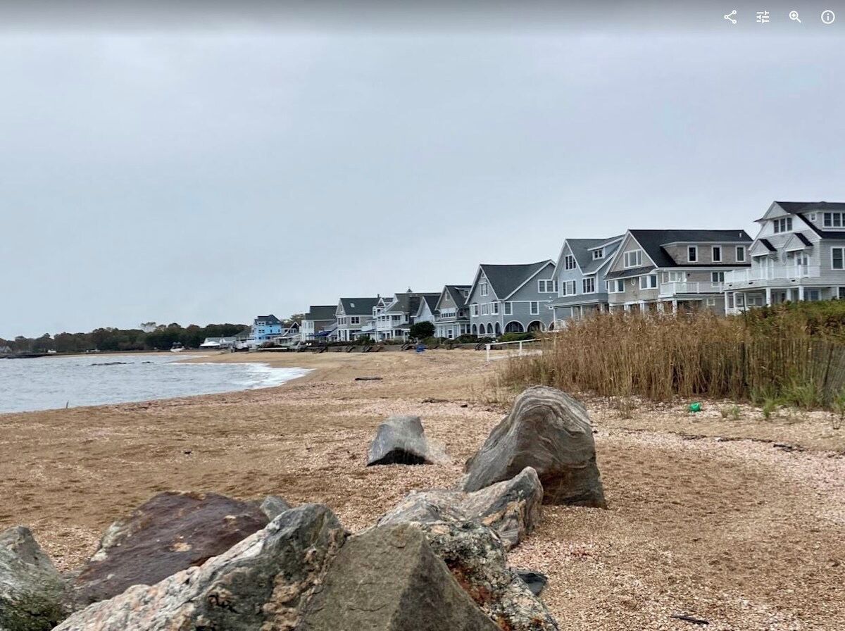 Ein Küstenwohngebiet mit Häusern entlang des Strandes, einem Sandstrand und großen Felsen im Vordergrund.