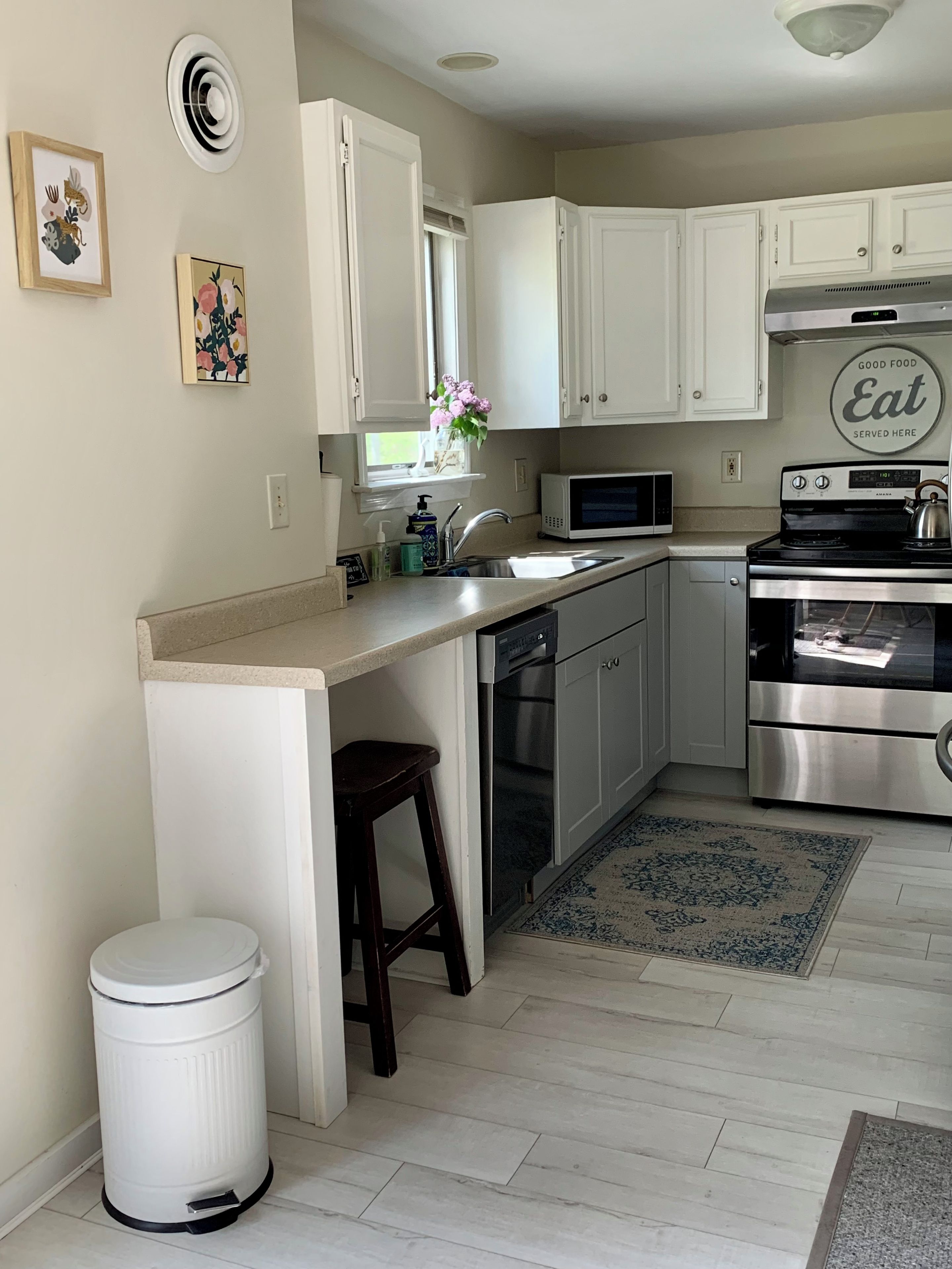 Una cocina compacta con gabinetes blancos, una estufa de acero inoxidable, un microondas y un lavamanos.