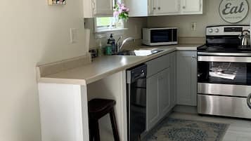 Una cocina compacta con gabinetes blancos, una estufa de acero inoxidable, un microondas y un lavamanos.
