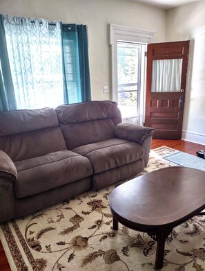 A living room with a sofa and a coffee table, a patterned rug, a door, and a window with curtains. - Comfortable 2-bedroom apartment in tranquil Richfield Springs with AC (Richfield Springs)