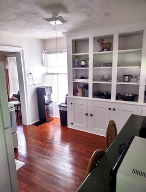 A kitchen with wooden flooring, white cabinetry, and a built-in shelving unit with various kitchen items. - Comfortable 2-bedroom apartment in tranquil Richfield Springs with AC (Richfield Springs)