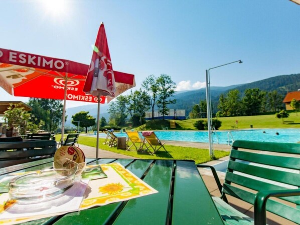 A poolside area with a table, chairs, and an umbrella. - One-bedroom Cabin (Sankt Georgen am Kreischberg)