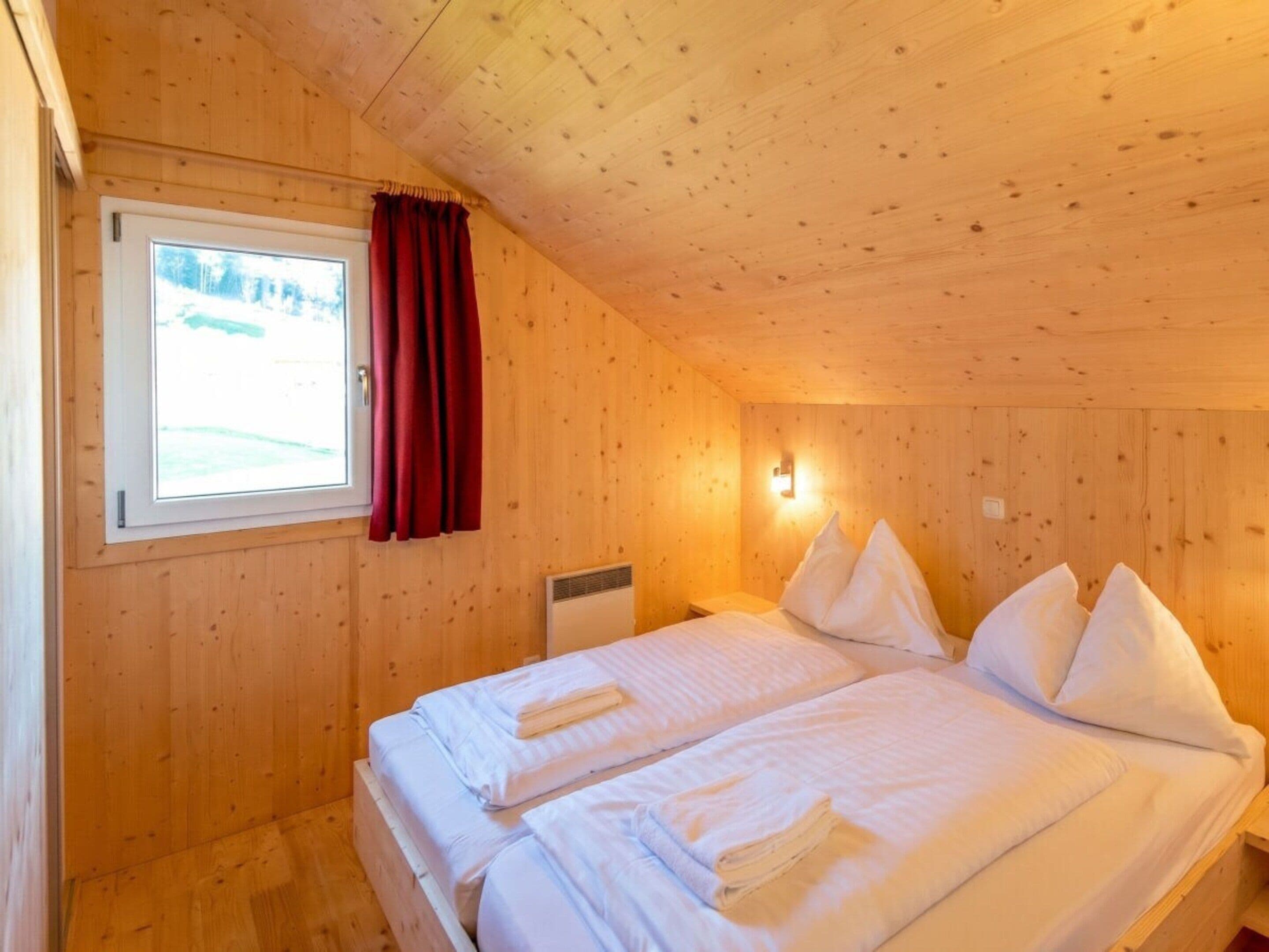 Una stanza in legno con un letto, una finestra e una lampada a parete.