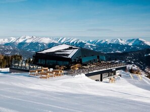 A modern building with a ski slope in the foreground and snow-covered mountains in the background. - One-bedroom Cabin (Sankt Georgen am Kreischberg)