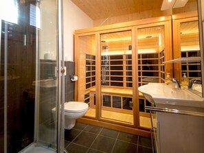 A modern bathroom with a glass shower enclosure, a white toilet, and a wooden vanity with a mirror. - One-bedroom Cabin (Sankt Georgen am Kreischberg)