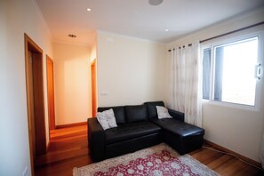 Una sala de estar con un sofá modular negro, un tapete estampado y un ventanal con cortinas.