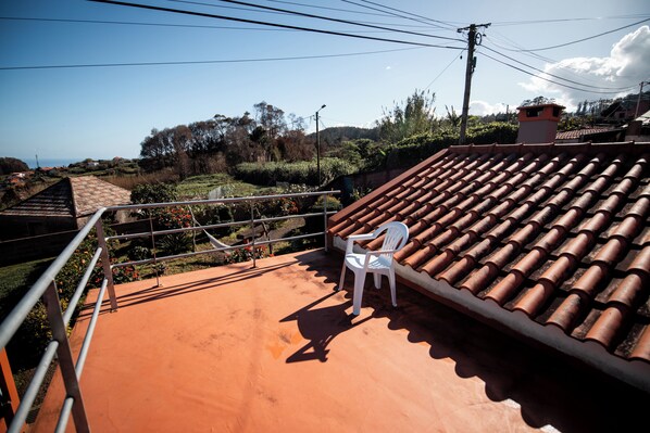 Una terraza con una silla de plástico blanca, techo de tejas y vista a un paisaje montañoso.