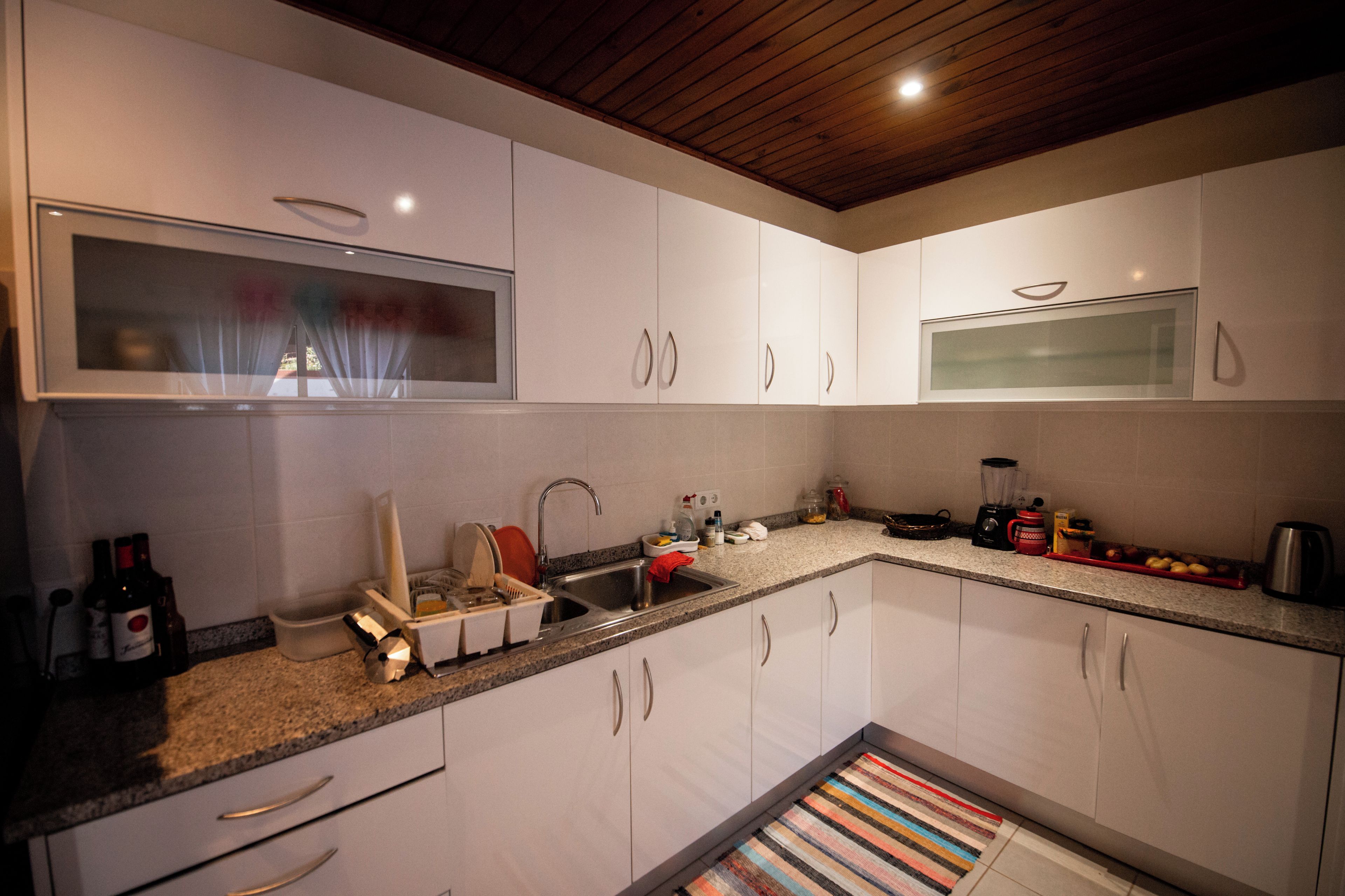 A modern kitchen with white cabinets, a granite countertop, and a wooden ceiling.