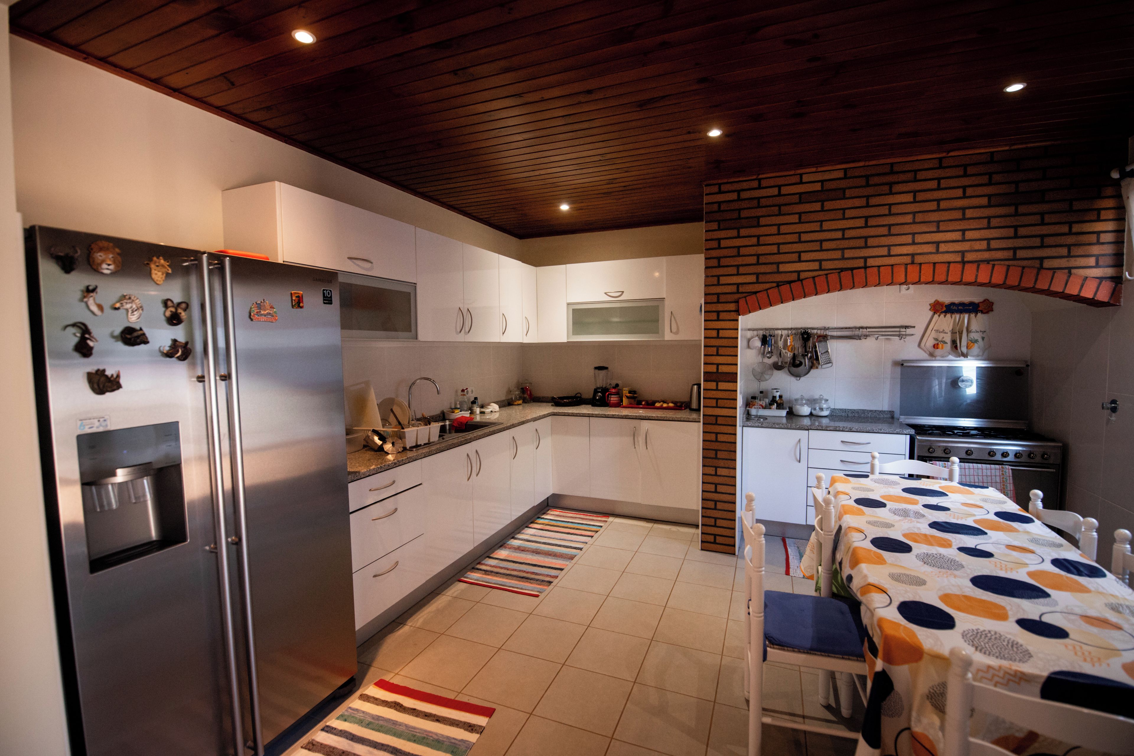 A modern kitchen with white cabinets, a stainless steel refrigerator, a built-in microwave, and a brick wall.