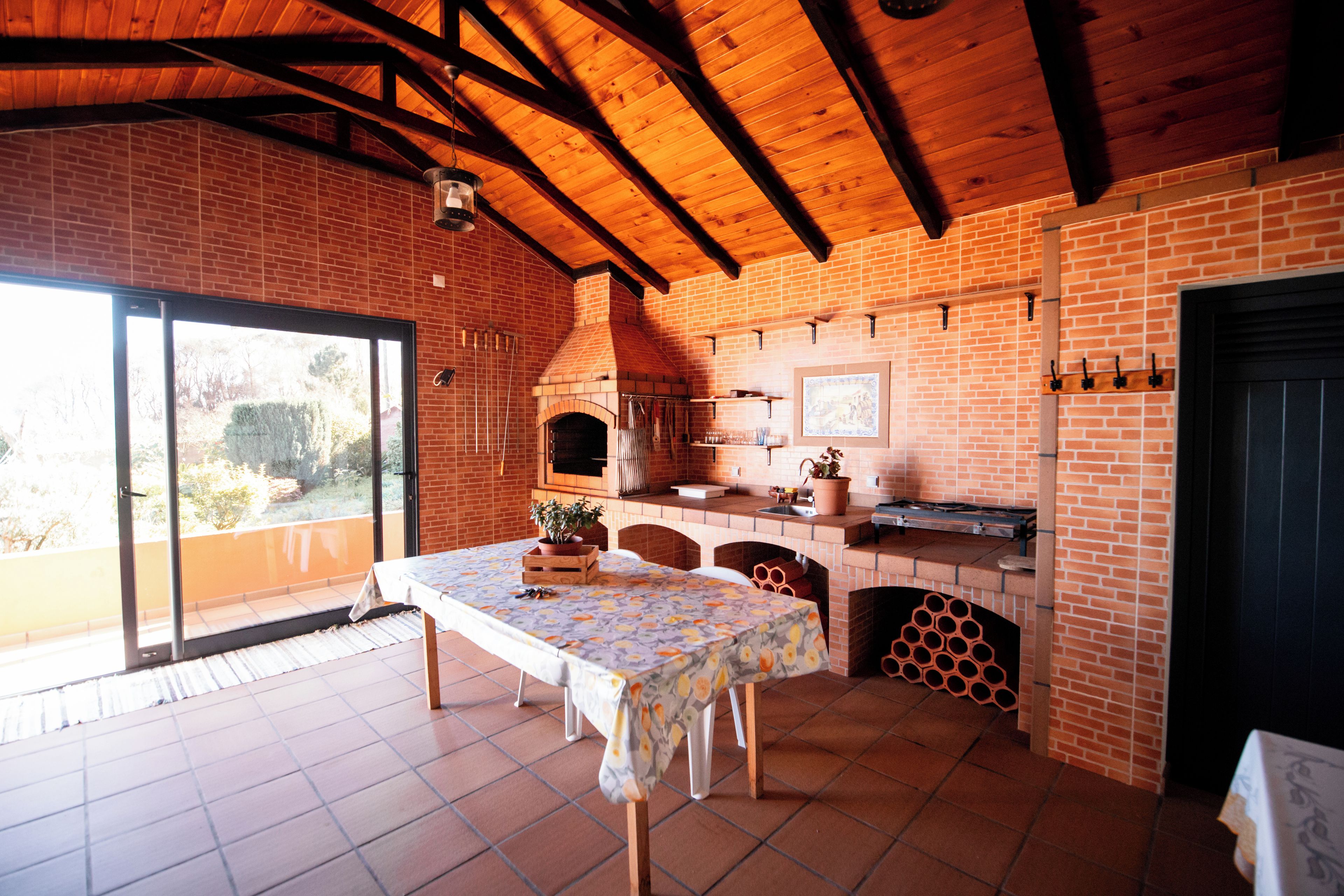 A rustic kitchen with a brick wall, wooden beams, and a tiled floor.