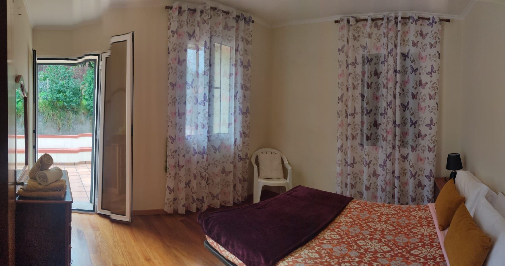 Une chambre avec un lit, une chaise, une petite table avec des serviettes et une vue sur l’extérieur, visible à travers la porte.