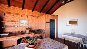 A kitchen with a brick wall, wooden beams, a sink, a stove, and a dining area with a table and chairs.