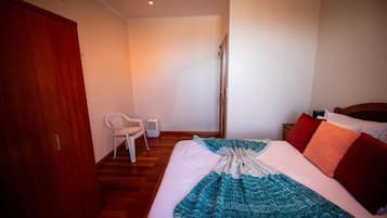 Une chambre à coucher avec un lit, une armoire en bois, une chaise blanche et une table de chevet avec une lampe.