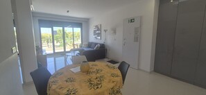 Quarto com mesa de jantar, cadeiras, sofá e vista através de grandes janelas.