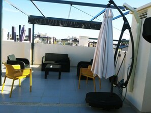 A rooftop terrace with a black sofa, two yellow chairs, a white umbrella, and a black suitcase. - Apartamento Playa Elisa Mil Palmeras (Pilar de la Horadada)