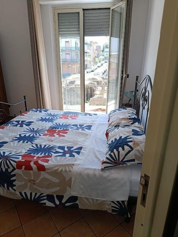 A room with a bed, a window, and a view of buildings outside.