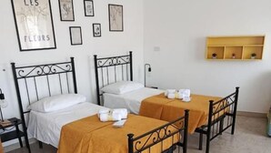 Een kamer met twee bedden, elk met hoofdeinde en nachtkastje. Er hangen afbeeldingen in lijsten aan de muur en een plank boven de bedden.