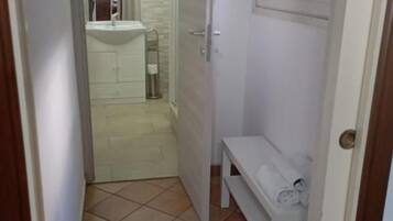 Un couloir étroit avec un banc blanc, une porte et un sol carrelé.