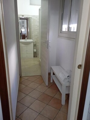 A narrow hallway with a white bench, a door, and a tiled floor. - Misterbeb (Misterbianco)
