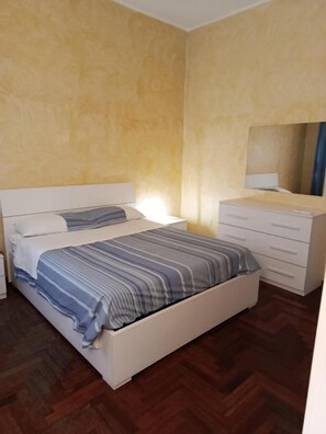 A bedroom with a bed, a bedside table, a dresser, and a mirror.