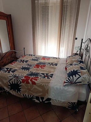 Un dormitorio con cama, espejo y ventana con cortinas.