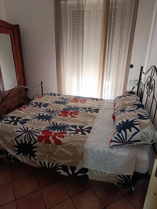 Un dormitorio con cama, espejo y ventana con cortinas.