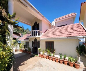 A two-story house with a red-tiled roof, a balcony, and potted plants in the courtyard. - Deluxe Aysha Stay Inn (Kodaikanal)