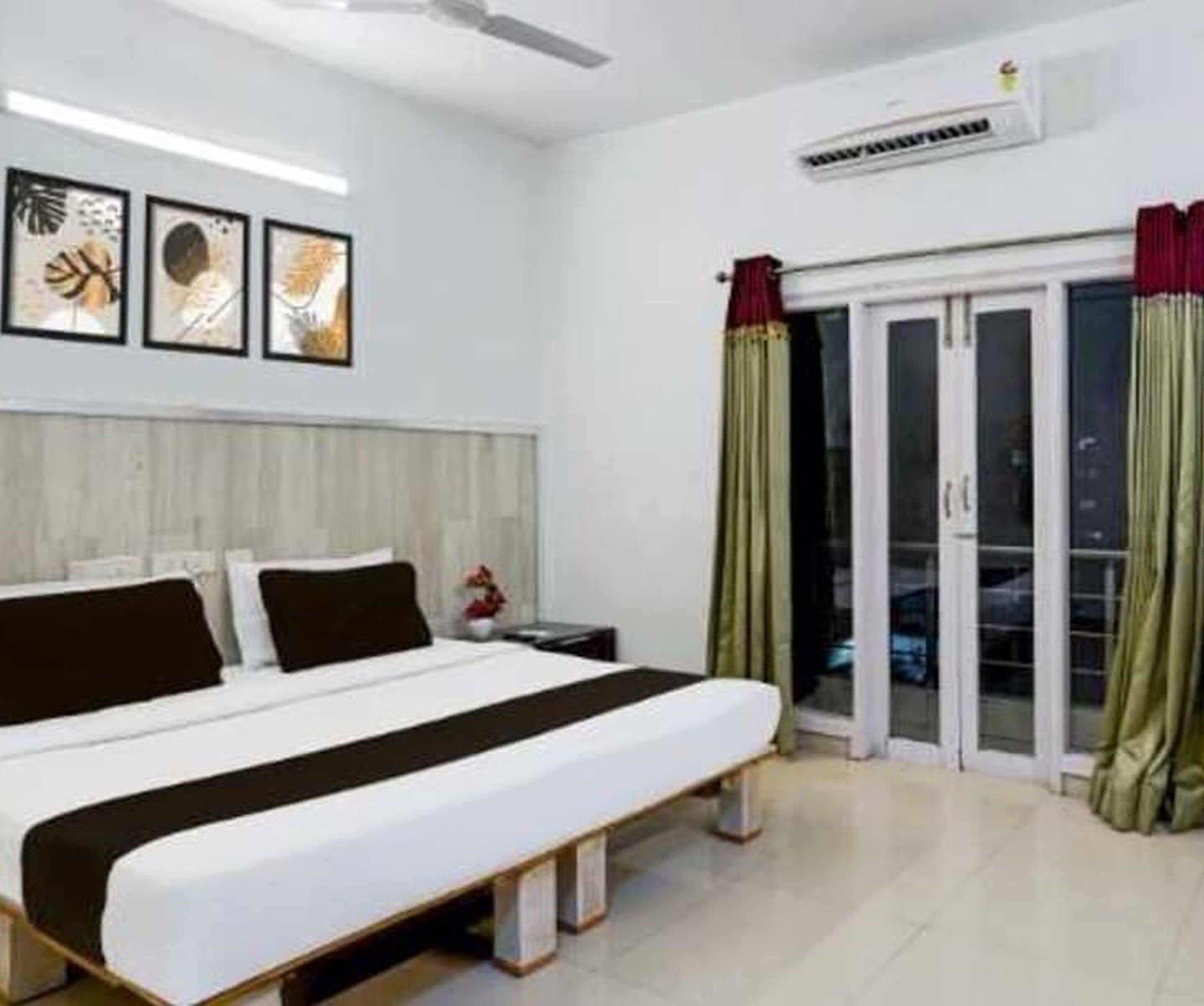 Una camera d'albergo con un letto, un comodino, un condizionatore d'aria a parete e una porta scorrevole in vetro che dà su un'area esterna.