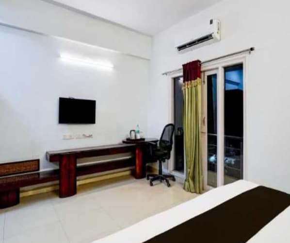A hotel room with a bed, a desk with a chair, a flat-screen TV, and a window with curtains. - Deluxe Aysha Stay Inn (Kodaikanal)
