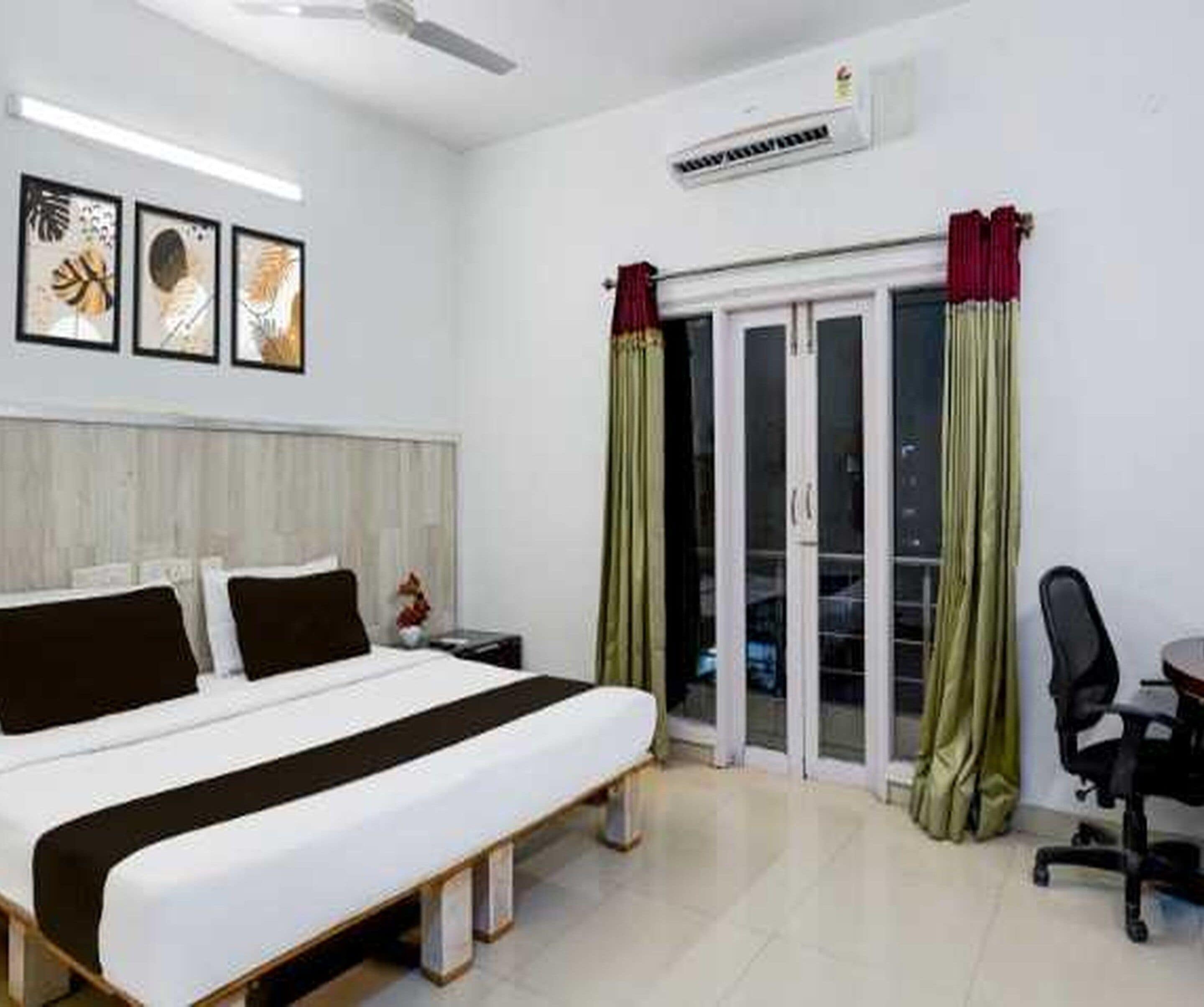 A hotel room with a bed, a desk, and a chair. There is a window with curtains, and a ceiling fan is visible.