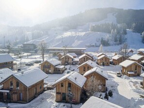 Eine Gruppe Holzhütten mit schneebedeckten Dächern, eingebettet in eine verschneite Winterlandschaft mit Bergeln im Hintergrund.